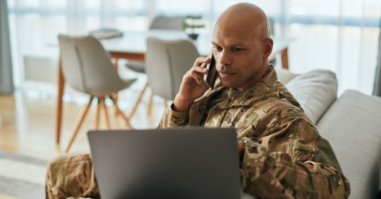 African American military member looking at his laptop while on his cell phone